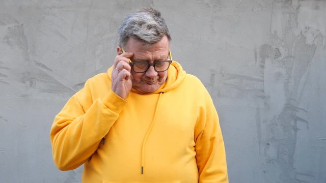 Aged man in bright clothes than upset, takes off his glasses and cries.