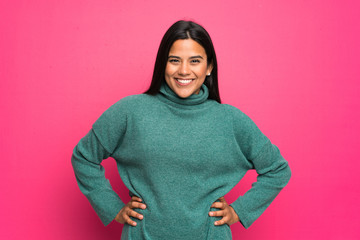 Young Colombian girl with green sweater posing with arms at hip and smiling