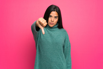 Young Colombian girl with green sweater showing thumb down with negative expression