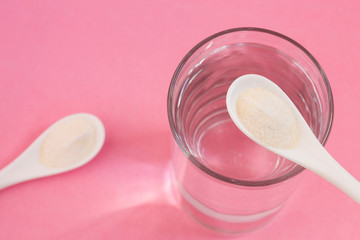 Collagen protein powder in the spoon. Glass of water