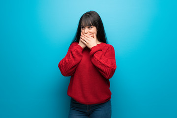 Woman with red sweater over blue wall covering mouth and looking to the side