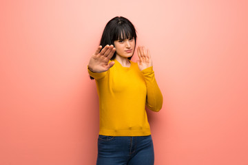 Woman with yellow sweater over pink wall nervous and scared stretching hands to the front
