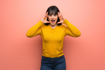 Woman with yellow sweater over pink wall with surprise expression