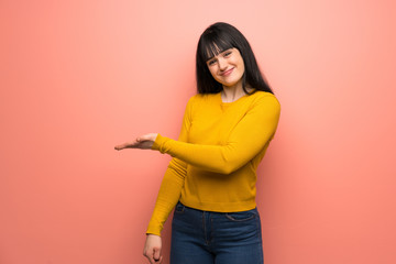 Woman with yellow sweater over pink wall presenting an idea while looking smiling towards