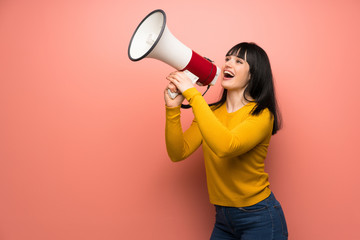 Woman with yellow sweater over pink wall shouting through a megaphone