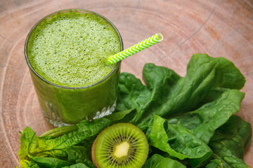Green smoothie in glass with straw, kiwi and spinach, healthy drink, top view, wooden background