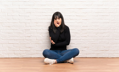 Woman sitting on the floor surprised and shocked while looking right