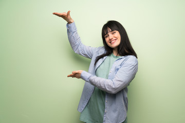 Young woman over green wall holding copyspace to insert an ad