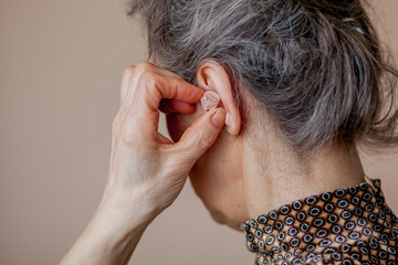 closeup senior woman inserting hearing aid in her ears