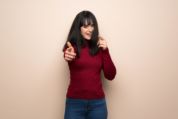 Young woman with red turtleneck pointing to the front and smiling