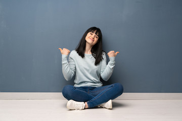 Woman sitting on the floor giving a thumbs up gesture and smiling