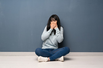 Woman sitting on the floor covering mouth and looking to the side