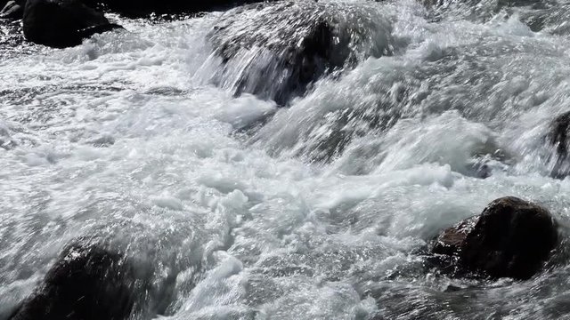 A hand held, extreme close up shot of the water foaming over the rocks, while flowing downwards.