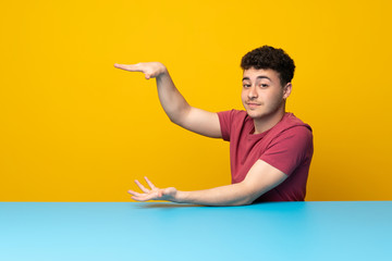 Young man with colorful wall and table holding copyspace to insert an ad