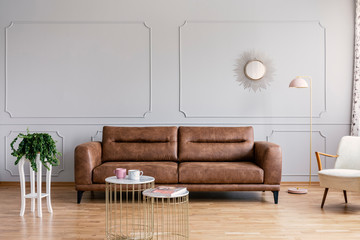 Real photo of a brown sofa, plant on a stool and metal coffee tables in a living room interior