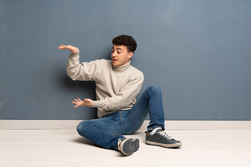 Young man sitting on the floor holding copyspace to insert an ad