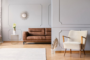 Real photo of a spacious living room interior with a white rug, armchair and leather sofa