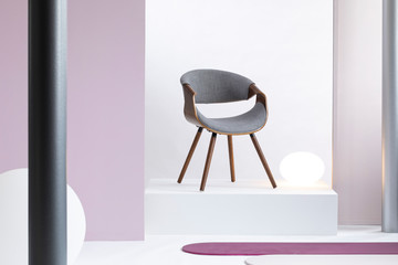 Real photo of a simple, white and purple room interior with a gray chair on a podium