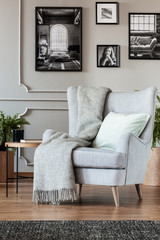 Comfortable grey armchair with cozy blanket and pillow in trendy living room interior with black and white posters on the wall