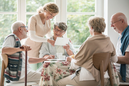 Group of seniors drinking tea together. Nurse is showing a photo to her female patient
