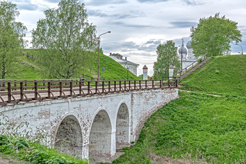 Fototapeta na wymiar Old city bridge over the moat and earthen ramparts. Belozersky Kremlin, Vologda region, city of Belozersk