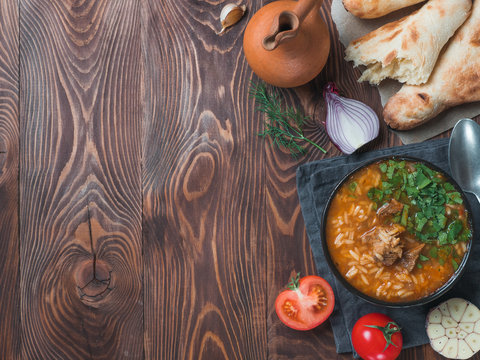 Traditional Georgian kitchen Kharcho soup with meat,rice,fresh cilantro.Spicy soup Kharcho on wooden table with traditional bread Shotis Puri,vintage wine jar,vegetables. Copy space for text. Top view