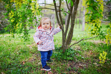 One year old girl standing next to a tree