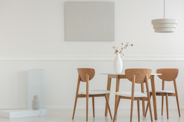 Spacious dining room interior with wooden chairs at desk and grey painting on the wall