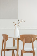 Closeup of flowers in white vase on wooden dining table with chairs