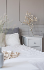 Bedside table with flowers in glass vase next to bed with white sheets