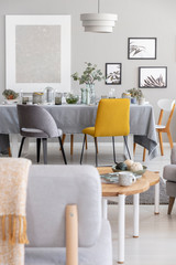 Grey and mustard chairs placed by the dining table with fresh plants, glasses and decor in real photo of small bright flat with posters