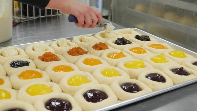 Walking Around Tray Of Uncooked Fruit Kolachies While Woman Adds Filling To Last Row. Woman adds fruit filling to kolaches before baking them.