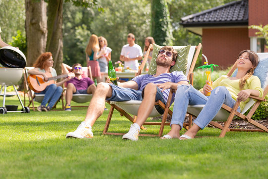 Smiling woman and man relaxing on sunbeds during grill party in the garden