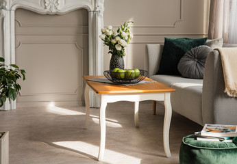 Roses in vase and apples in bowl on wooden coffee table in grey living room interior