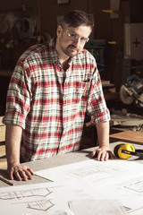 Professional engineer with glasses at table with project and protective headphones