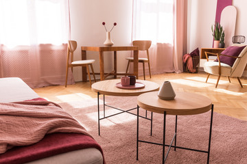 Round wooden tables on pink carpet in apartment interior with couch and armchair. Real photo