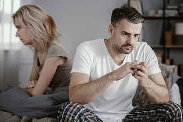 Man in pajamas sitting in bed and taking off his wedding ring after his wife announced that she...