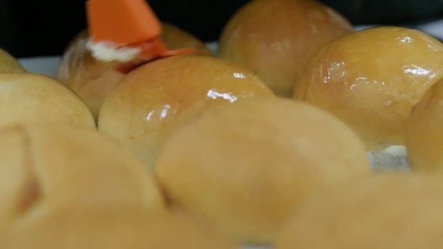woman coats the top of hot kolaches with butter in slow motion. Baker brushes top of fresh kolaches with melted butter.