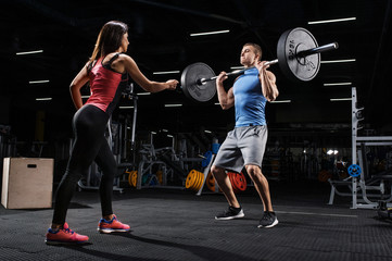 Sport, fitness, teamwork and couple concept. Female personal trainer motivating athlete training with barbell in a gym.