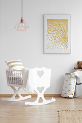 Copper lamp above white cradle in simple child's bedroom interior with yellow poster. Real photo