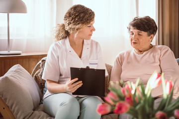 Young nurse helping elderly lady with filling in the forms in the nursing home