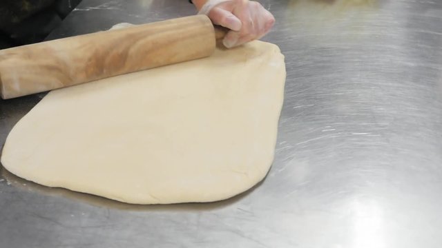 woman presses out dough with wood rolling pin. Woman uses wooden rolling pin to flatten dough.