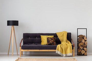 Yellow blanket on settee between lamp and logs of wood in grey apartment interior. Real photo