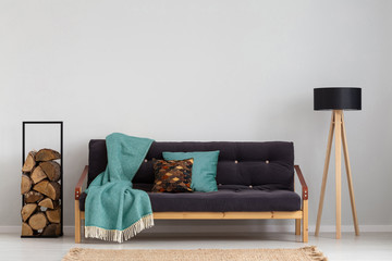 Blue blanket on sofa in grey simple living room interior with lamp and logs of wood. Real photo
