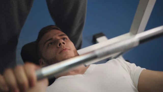 Young bodybuilder lifting barbell lying on a baench in a gym.
