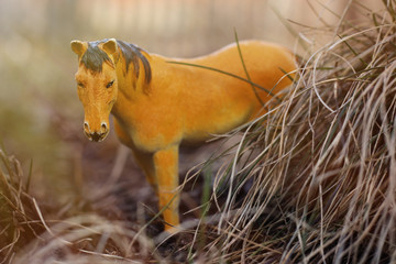 toy horse in nature photographed as real among the dry grass like haystacks