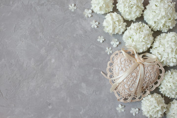 Fototapeta na wymiar Gray plaster background with white flowers of decorative viburnum buldenezh and lace heart
