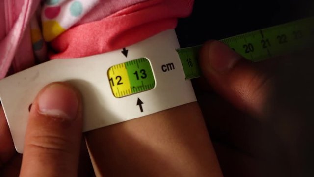 A hand held, extreme close up shot of a person measuring the arm of a child with a centimetre.