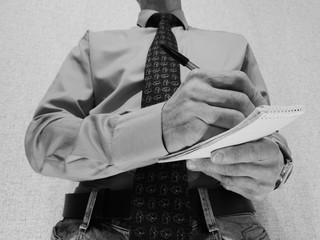 A business man is writing in a notebook. Business man and notebook
