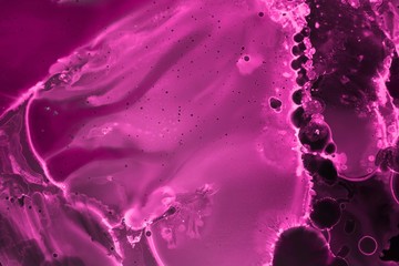 Pink alcohol ink texture with abstract washes and paint stains on the black paper background.	